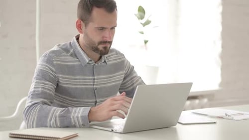 Frustrated Man Working at Computer in Bright Office