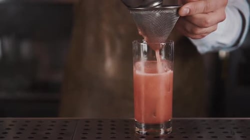 Bartender Straining Pink Cocktail Into Glass