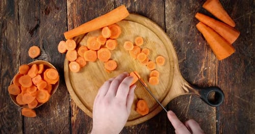 Person Cuts Carrots on Cutting Board with Knife