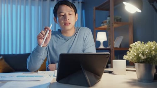 Asia freelance businessman focus work pen write on tablet computer busy with full of graph paperwork