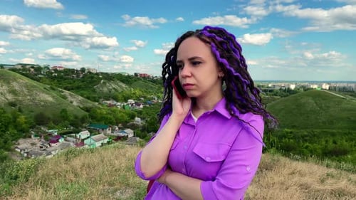 Young beautiful woman talking on mobile phone, standing in hilly terrain.