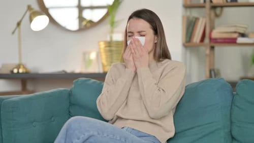 Sick Young Woman Sneezing Sitting on Sofa