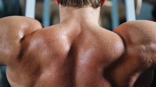 4K Caucasian man bodybuilder pulling up body weight lifting at gym.