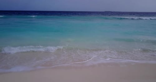 Daytime overhead tourism shot of a sunshine white sandy paradise beach and blue water background in