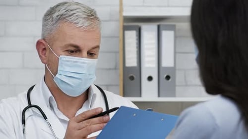 Doctor Wearing Face Mask Talking With Patient In Clinic Indoors