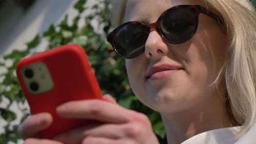 Woman using mobile phone in a garden with wall and doors on background