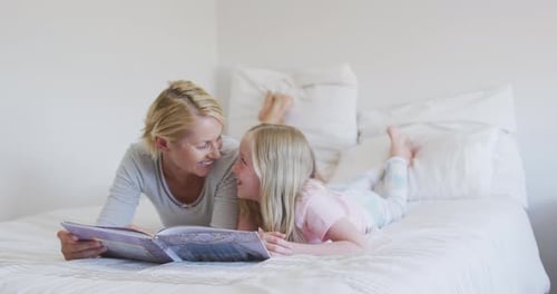 Side view of a Caucasian woman reading a story to her daughter on bed