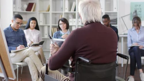 Group Listens to Speaker in Wheelchair in Office