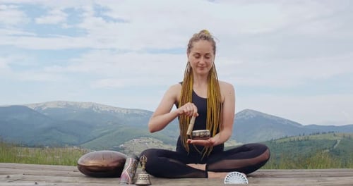Woman Sits Playing Singing Bowl in Mountain Setting