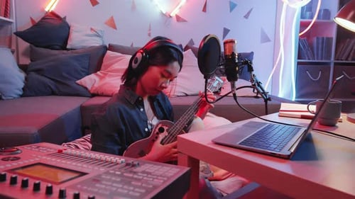 Young Asian Female Musician Recording Guitar Song in Home Studio