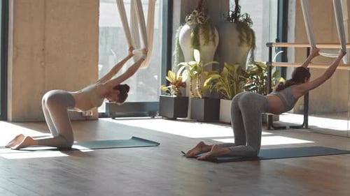 Women Doing Aerial Yoga Stretch in Bright Studio