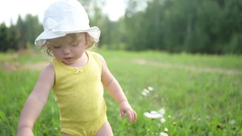 Little Funny Cute Blonde Girl Child Toddler in Yellow Bodysuit and White Hat Walking in Field with