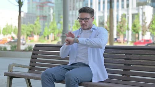 Man Scrolling Through Smart Watch Applications on Bench