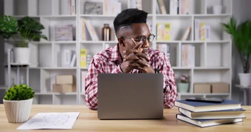 Young Adult Thinks at Desk with Laptop