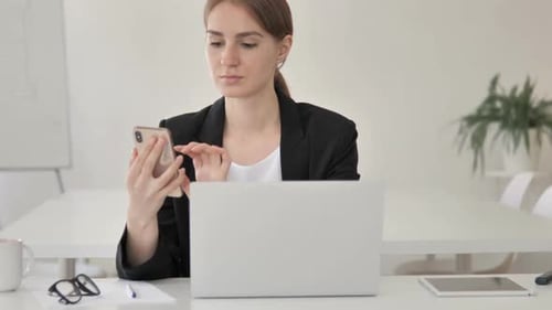 Woman Using Phone at Desk with Laptop