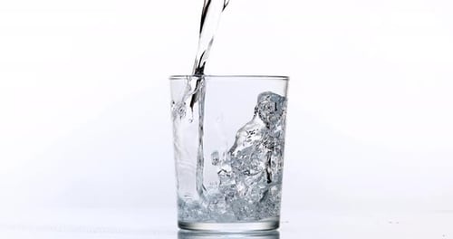 900096 Se vierte agua en un vaso sobre un fondo blanco, Cámara lenta 4K