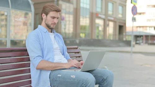 Young Adult Using Laptop on City Bench