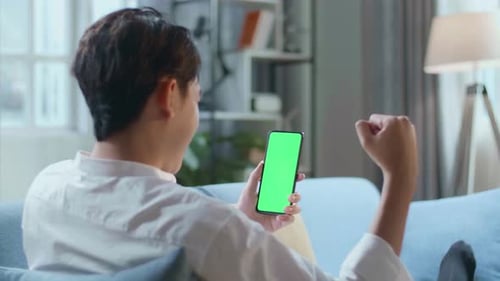 Man Celebrating While Lying On Sofa And Using Green Screen Smartphone In The Living Room