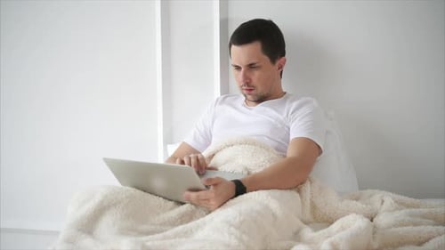 Homme naviguant sur le Web sur un ordinateur portable lorsqu'il est allongé dans son lit