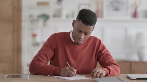 African Man Writing on Paper in Office