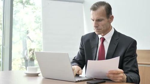 Geschäftsmann liest Dokumente und arbeitet an Laptop-Papieren