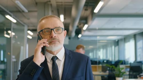 Senior Businessman Walking in Office and Speaking on Phone