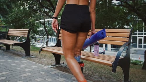 Disabled Woman Putting Fitness Mat on Bench Near Water Bottle and Going Away Close Up