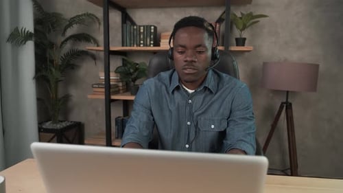 African Man Employee Works in the Office at the Computer. Black Businessman with Wireless Headset