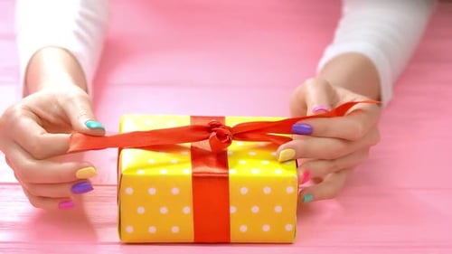 Hands Untying Yellow Birthday Present on Pink Surface