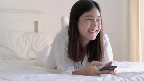 Woman Using Phone on Bed, Smiling