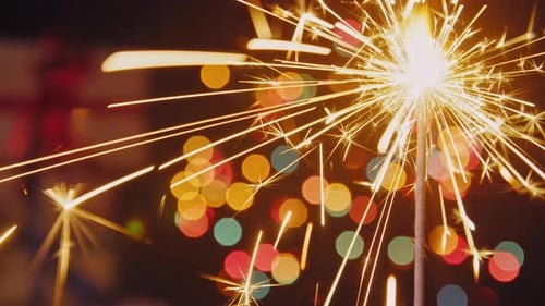 Close-Up Of Sparkler Glittering In Front Of Christmas Tree