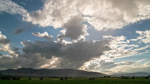 Timelapse of clouds moving through the sky over farmland as sun peeks through