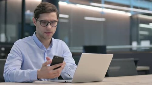 Young Adult Working with Laptop and Smartphone in Office