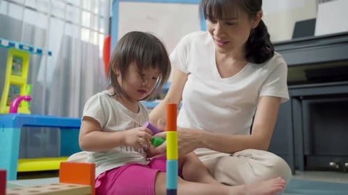 Asiatische glückliche Familie, schöne Mutter und kleines Mädchen spielen zusammen Spielzeug im heimischen Wohnzimmer