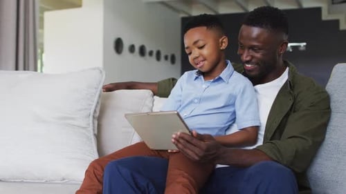 Father and Son Using Tablet on Sofa at Home