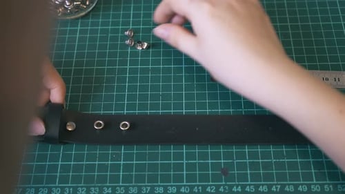 Un tailleur qualifié met des accessoires en métal sur une ceinture en cuir noir
