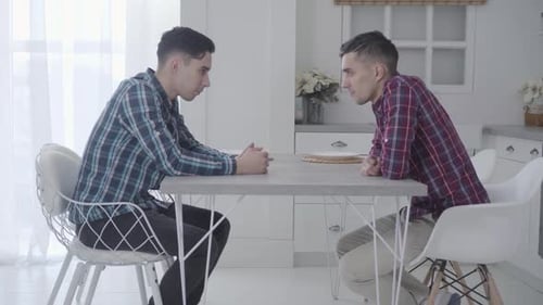 Two Young Men in Kitchen Having Serious Discussion