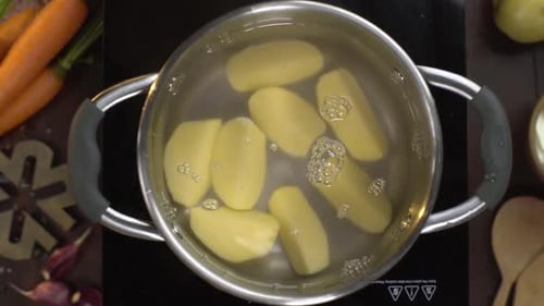 Vídeo Flat Lay: o cozinheiro joga batatas descascadas na água fervente, mesa de vegetais fervendo