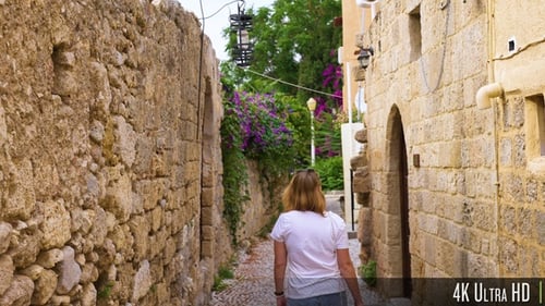 4K Following young woman walk down narrow cobblestone street with stone walls and houses