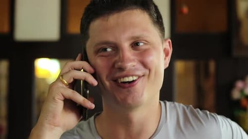A steady handheld close-up shot of a young white man, in his 30s , talking on the phone and smiling,