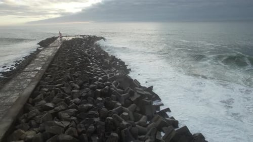 Waves Crashing on Rocky Jetty With Lighthouse at Sunset