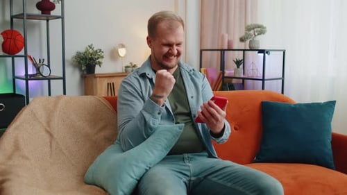Man Celebrates Good News on Smartphone at Home