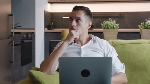 Thoughtful man works on laptop at home