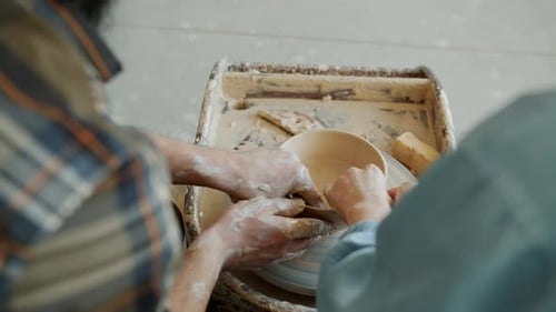 Back View Slow Motion of Male and Female Hands Shaping Pot From Clay on Throwing Wheel Working