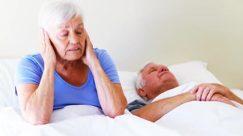 Femme irritée se couvrant les oreilles tandis que l'homme ronflait sur le lit