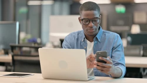Young Adult Uses Phone and Laptop in Office