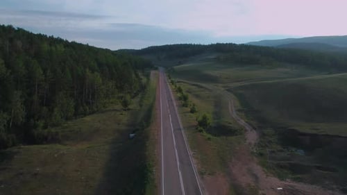 AERIAL, TOP DOWN: Dark Colored Car Driving Down an Asphalt Road Crossing the Vast Forest on a Sunny