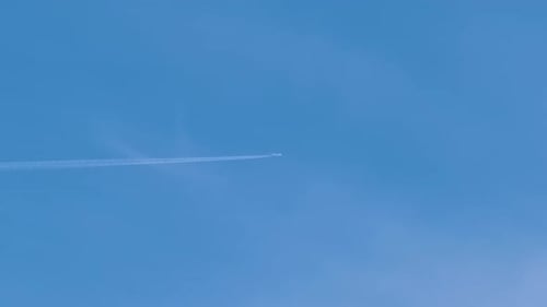 Avión jet de pasajeros lejanos volando a gran altitud en un cielo azul claro dejando rastros de humo blanco de