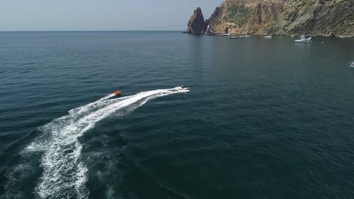 Jet Ski Tows Tube Along Coastline on Sunny Day