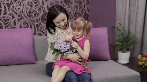 Mother and Daughter with Lilac Bouquet on Sofa